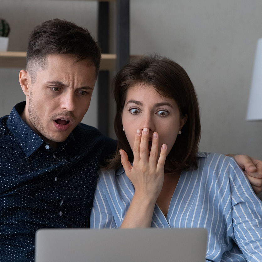 junges Paar vor Laptop mit erschrockenem Gesichtsausdruck